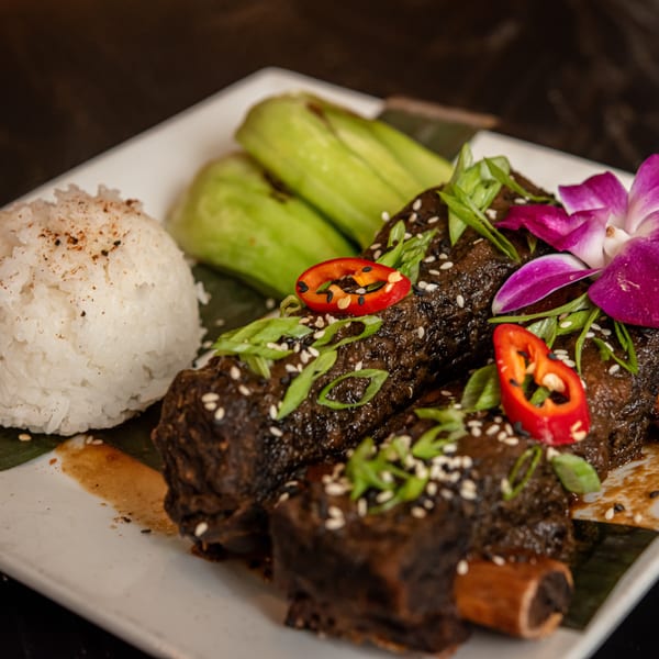 Braised short ribs with rice, bok choy, chili, green onions, sesame seeds, and an orchid.