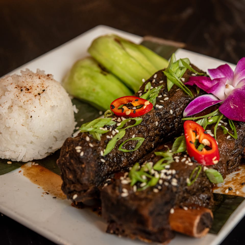 Braised short ribs with rice, bok choy, chili, green onions, sesame seeds, and an orchid.