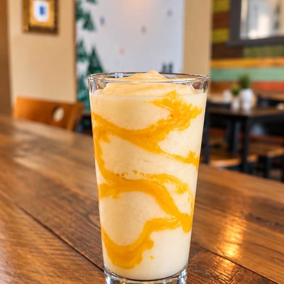 Tall glass of creamy orange-swirled dessert sits on a rustic wooden restaurant table.