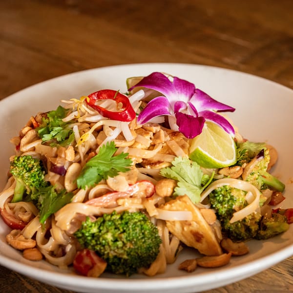 Pad Thai noodles with broccoli, cashews, bean sprouts, lime, and an orchid garnish.
